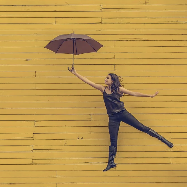 Woman with umbrella floats on yellow board wall